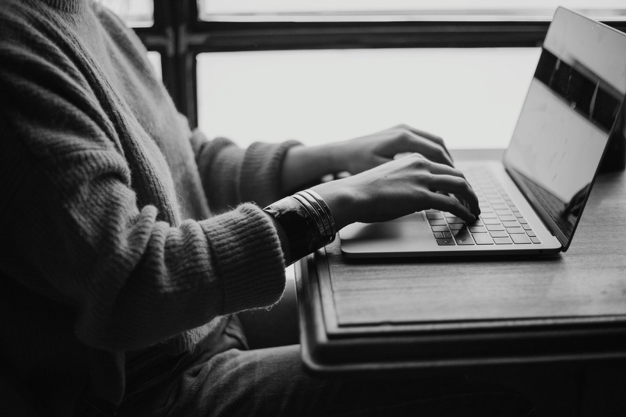 Hands typing on a laptop beside a window